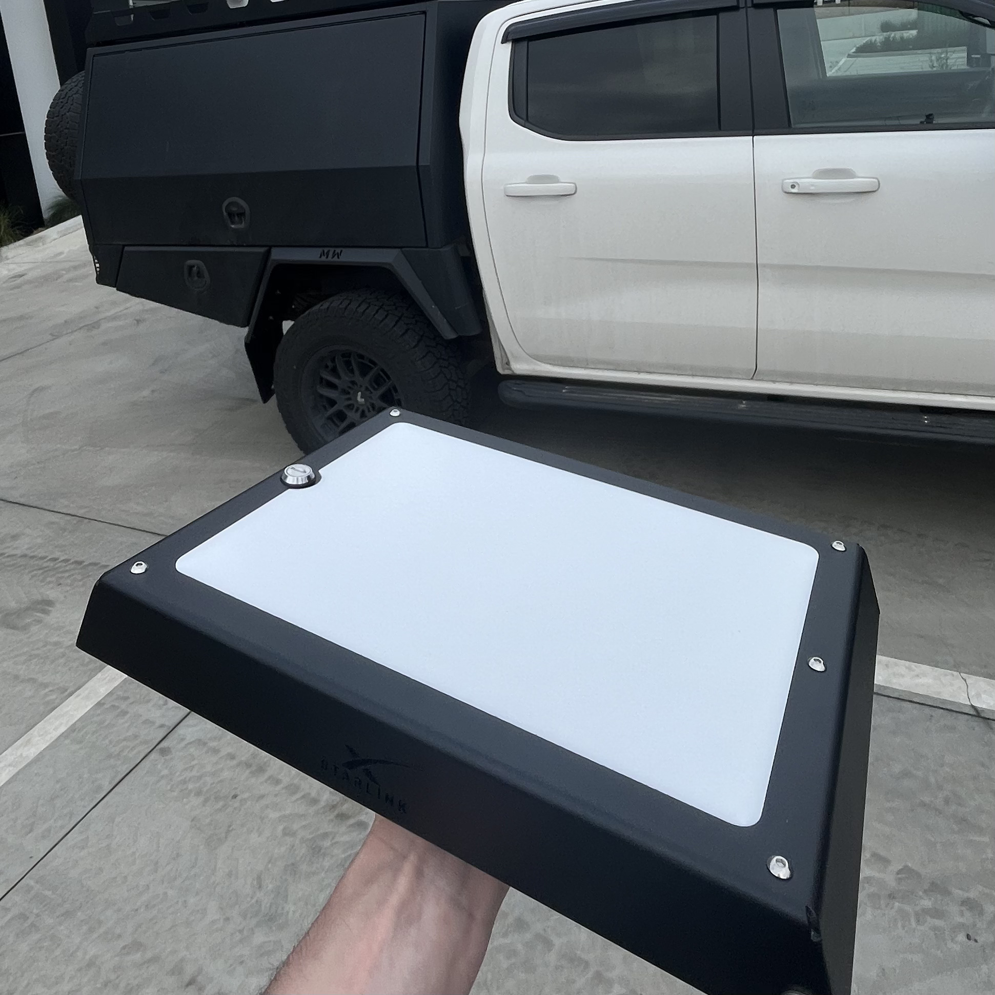 Black Power Hub held beside a white dual-cab utility with a black tray, showing how the textured powder coat and low profile sit against the vehicle